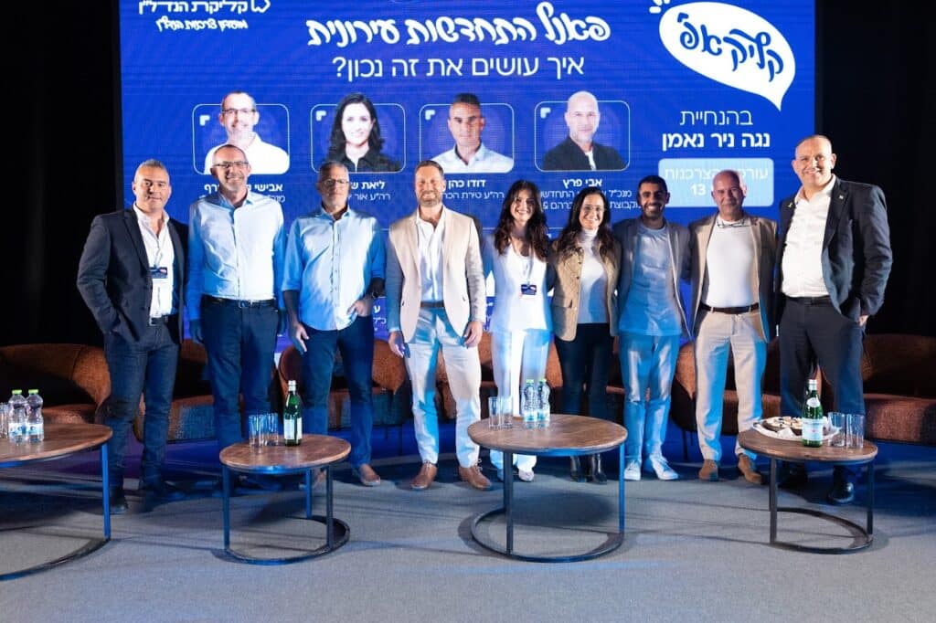 בר נעמני מדבר בפאנל מקצועי בכנס קליקאפ, אוחז מיקרופון ולבוש בחליפה בהירה.